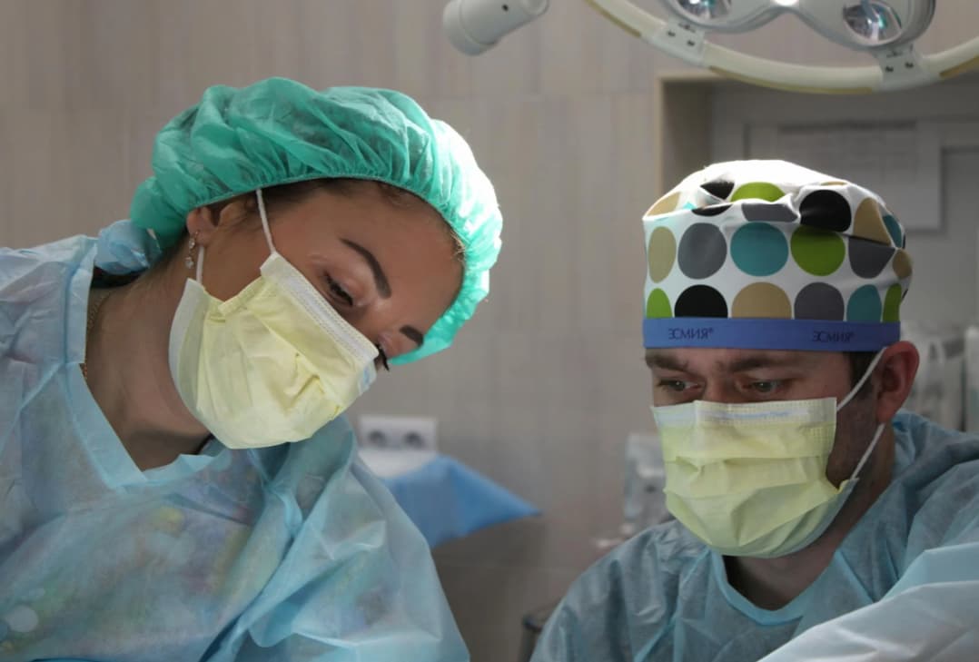 Two surgeons in scrubs and surgical caps focusing intently during a procedure